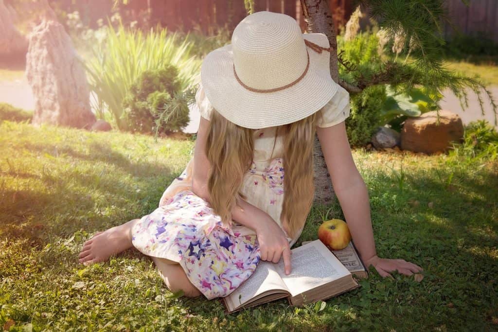 girl with hat sitting in sun reading a book